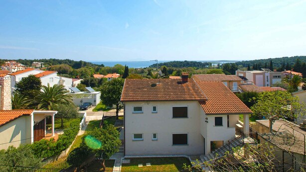 Un quartiere residenziale con un edificio a due piani, un piccolo giardino e vista sul mare.