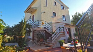 Una casa a due piani con un balcone, una scala che conduce al piano superiore e un piccolo spazio esterno arredato con tavolo e sedie.