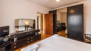 A modern bedroom with a large bed, a vanity with a mirror, a ceiling fan, and a dark wardrobe. - Holiday apartment with garden and barbecue (Banjole)
