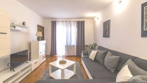 A modern living room with a flat-screen TV, a grey sofa, and a white coffee table. - Holiday apartment with garden and barbecue (Banjole)
