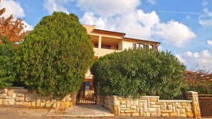 A two-story house with a stone wall entrance, a balcony, and a clear sky with clouds. - Holiday apartment with garden and barbecue (Banjole)