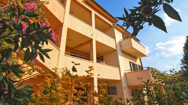 A multi-story building with balconies and a garden area with flowering plants. - Holiday apartment with garden and barbecue (Banjole)