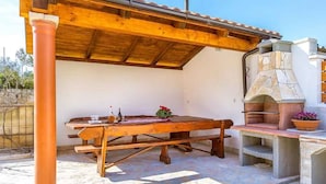 Eine Terrasse im Freien mit einem Holztisch, Stühlen, einem Steinofen und einer Pergola.