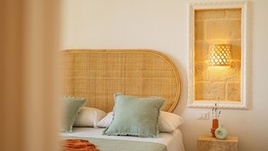 Een bed met een geweven hoofdbord, twee kussens, een nachtkastje met een vaas, en een wandlamp.