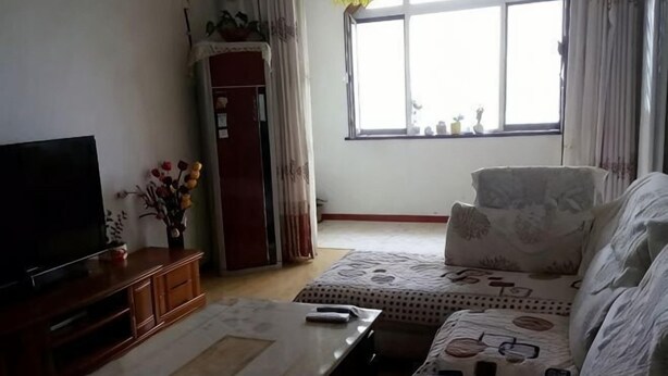 A living room with a flat-screen TV, a coffee table, a sofa, and a window with curtains. - Qingdao Golden Beach Chaoyang Seaview Apartment (Qingdao)