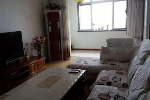 Een woonkamer met een flatscreen televisie, een salontafel, een bank en een raam met gordijnen.