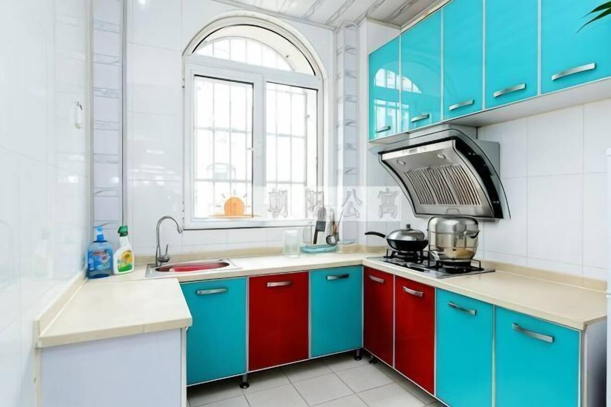 A kitchen with a window, white tiles, a stove, and cabinets.