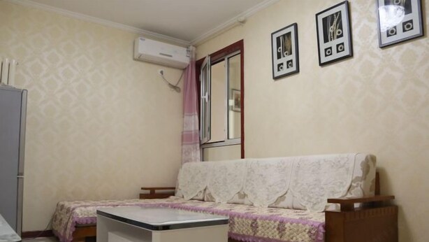 A small, neatly arranged room with a bed, a sofa, a table, and a mirror. - Qingdao Golden Beach Chaoyang Seaview Apartment (Qingdao)