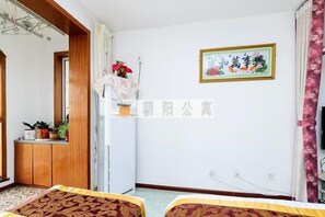 A hotel room with a bed, a small table with a plant, a white cabinet, and a wall-mounted picture. - Qingdao Golden Beach Chaoyang Seaview Apartment (Qingdao)