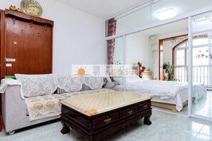 A room with a bed, a sofa, a wooden cabinet, and a window with curtains. - Qingdao Golden Beach Chaoyang Seaview Apartment (Qingdao)
