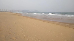 A beach with footprints leading to the water, a calm sea, and a hazy sky. - Qingdao Golden Beach Chaoyang Seaview Apartment (Qingdao)