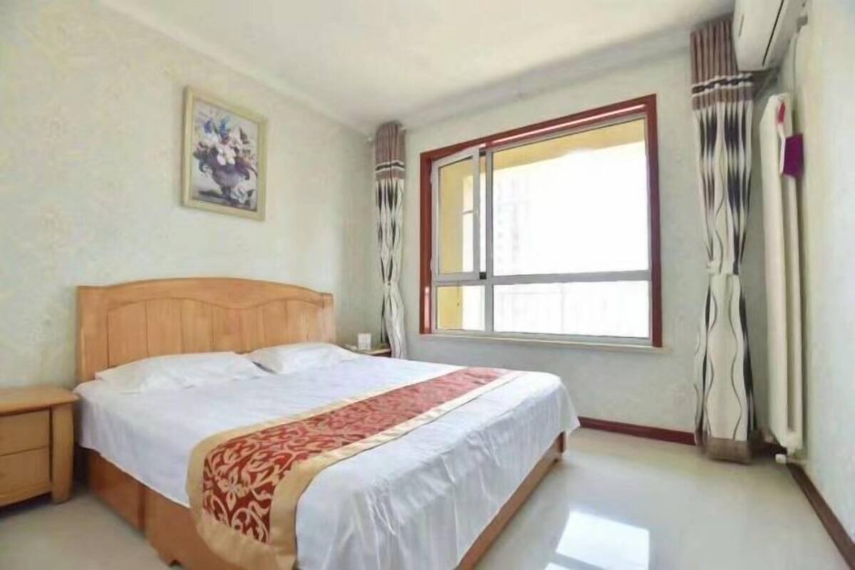 A bedroom with a wooden bed, a nightstand, a window with curtains, and a wall-mounted picture.