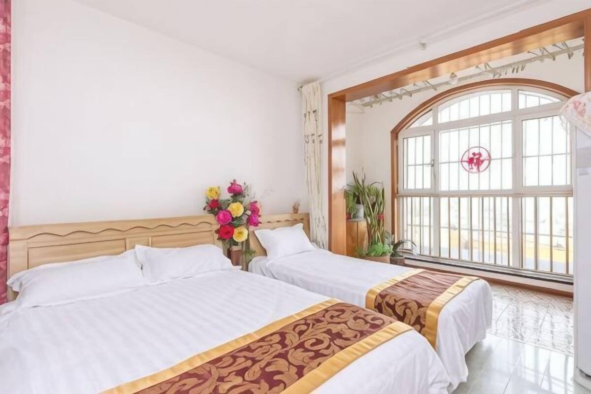 A hotel room with two beds, a large window with a view, and a floral arrangement on the nightstand.