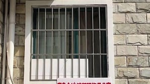 A window with metal bars, a stone wall, and a white pipe. - Qingdao Golden Beach Chaoyang Seaview Apartment (Qingdao)