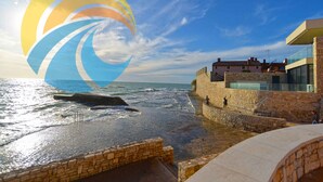 A coastal view with a stone wall and a modern building with glass windows.