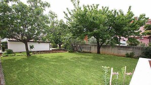 A well-maintained grassy yard with trees and a white building in the background.