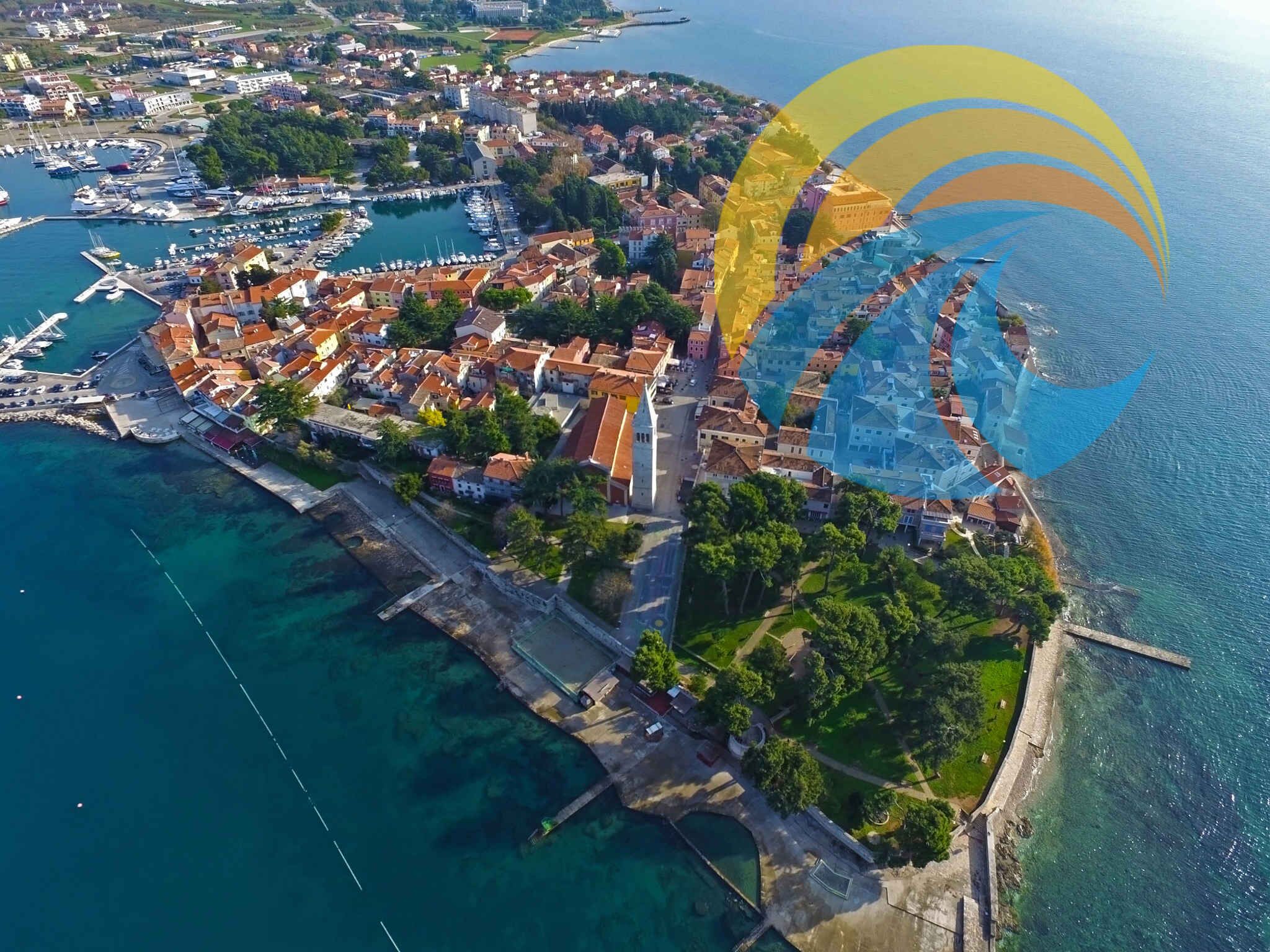 Vista aérea de uma cidade costeira com um porto de iates, edifícios históricos e uma igreja imponente.