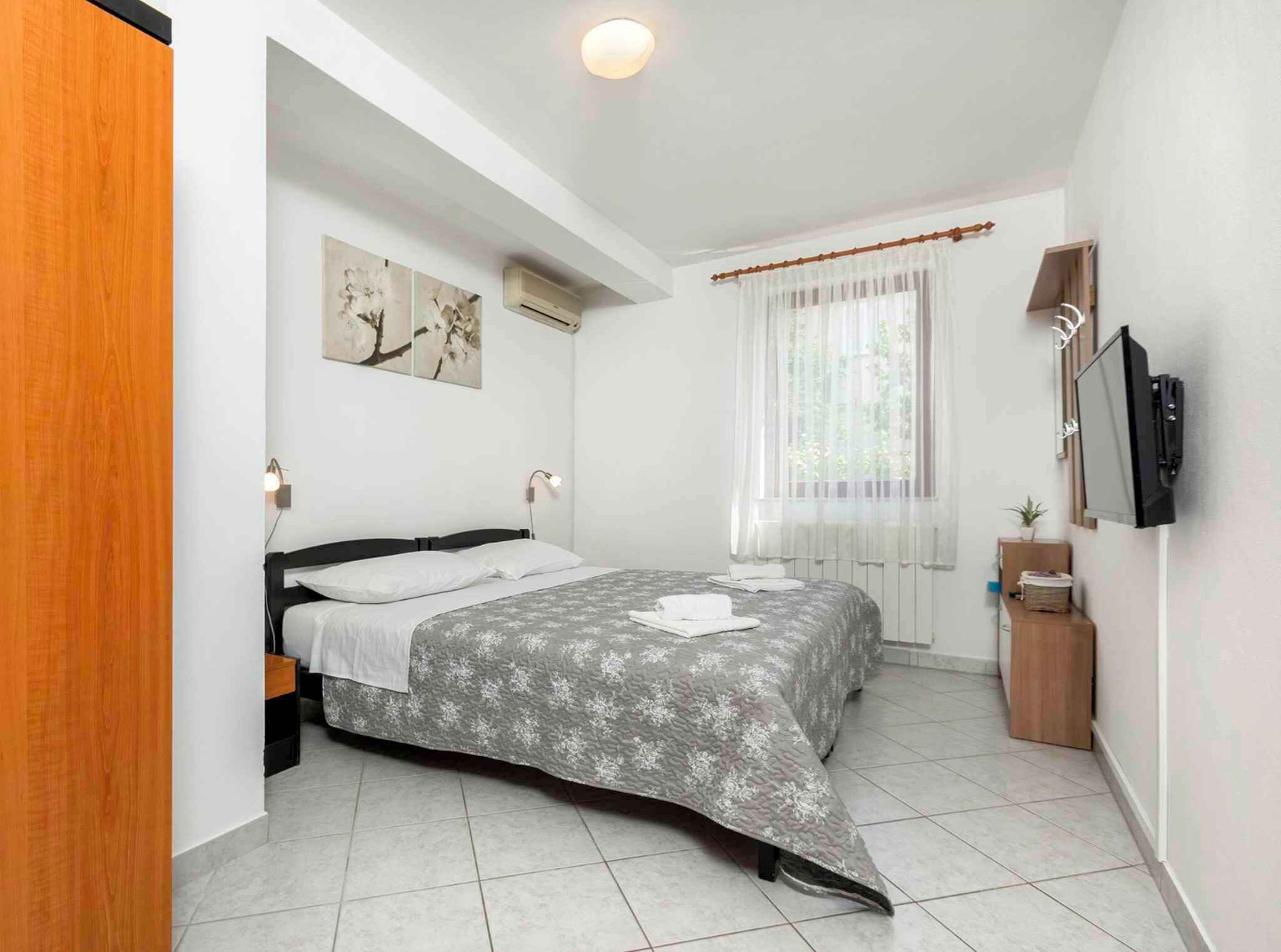 Una camera da letto con un letto, una TV, una finestra con tende e un condizionatore d'aria a parete.