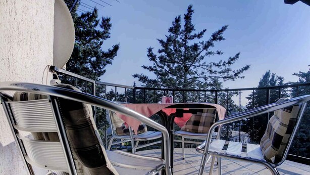Un balcon avec des chaises et une table en métal, donnant sur une zone boisée.