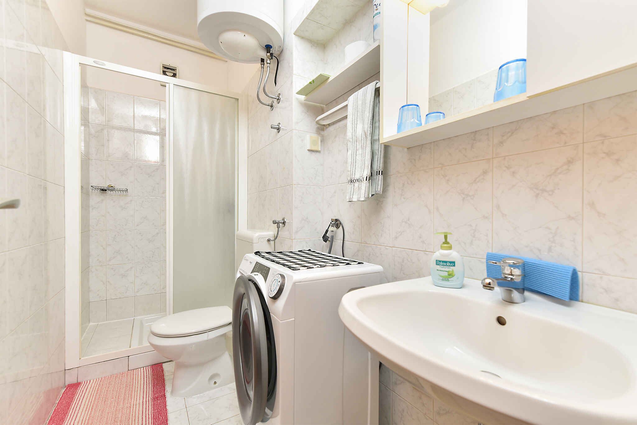 A bathroom with a shower, toilet, washing machine, and sink.