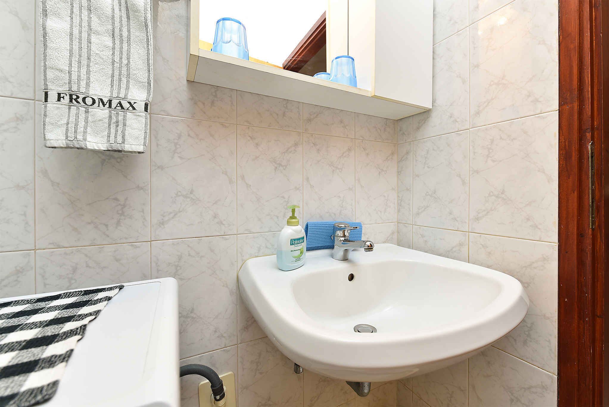 A bathroom with a white sink, a towel hanging on the wall, and a shelf with blue glasses.