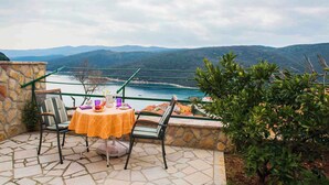 Une terrasse avec une table et des chaises offrant une vue panoramique sur la côte et les collines.