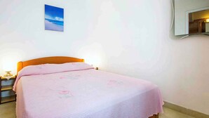 Une chambre à coucher comprenant un lit, une table de chevet, un miroir fixé au mur et un tableau représentant une scène de plage.