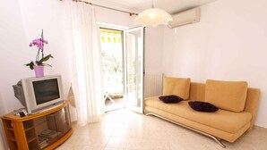 Una sala de estar con un sofá, un televisor sobre un mueble de madera y una ventana con cortinas.
