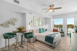 A modern bedroom with a bed, two green bar stools, a small table, and a ceiling fan.
