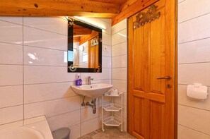 Un bany amb una porta de fusta, un lavabo blanc, un mirall i una petita estantella.