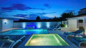 Piscina con fuente, sillas de descanso y pared de piedra.