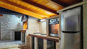 Cocina compacta con pared de piedra, techo de madera y electrodomésticos integrados, incluyendo refrigerador y horno.