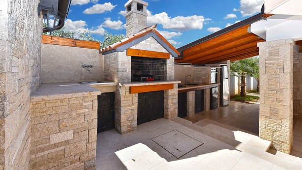Un área de cocina al aire libre con paredes de piedra, una chimenea y techo de madera.