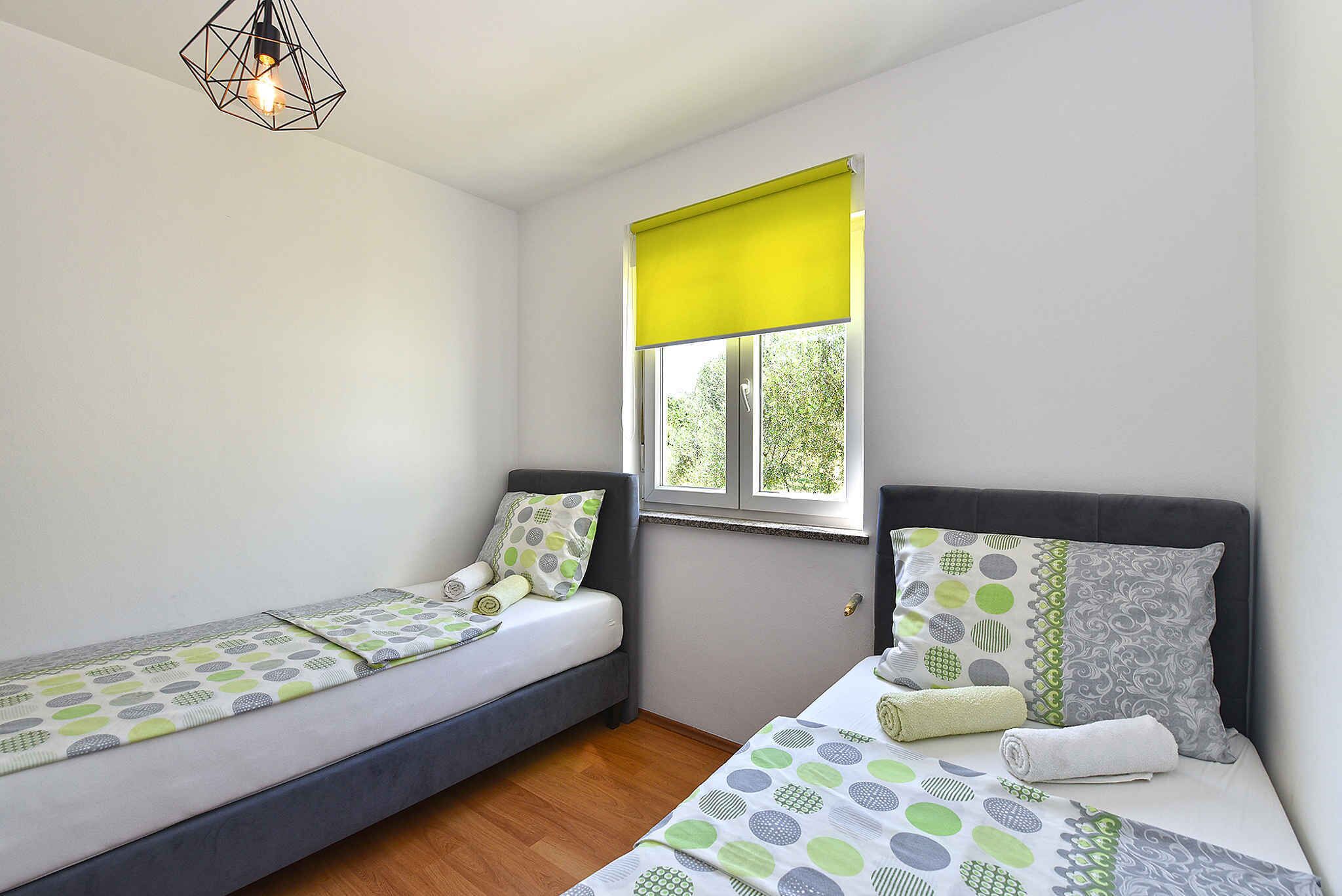 A room with two single beds, a window with a yellow blind, a hanging light fixture, and a wooden floor.