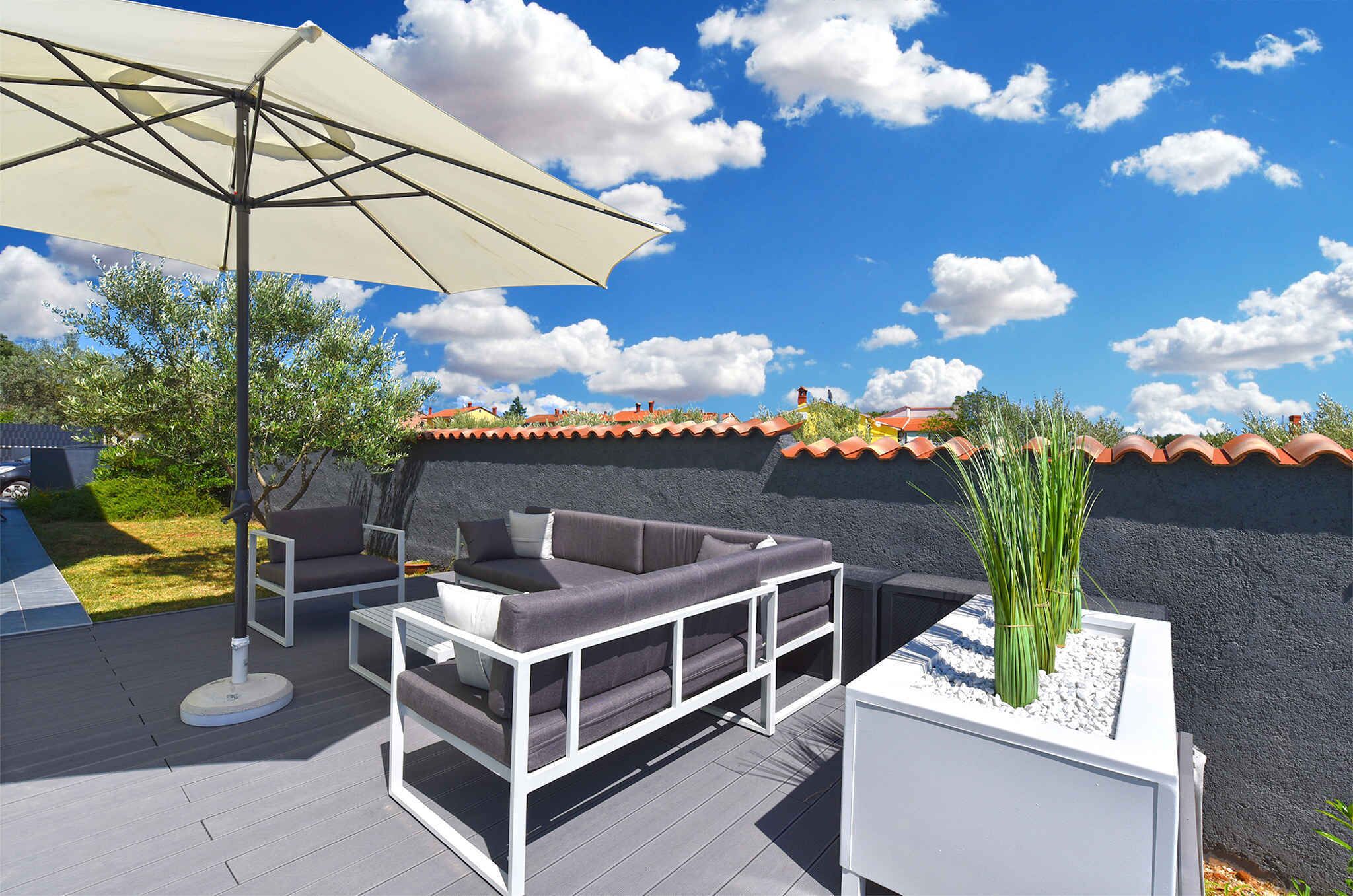 Eine Terrasse im Freien mit einer Sofagruppe, einem Tisch und einem großen Sonnenschirm.