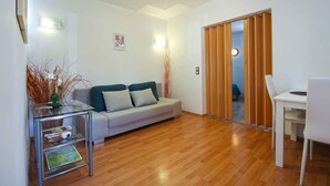 A modern living room with a glass coffee table, a grey sofa, a wooden floor, and a white dining table with a chair. - Holiday apartment with air conditioning (Pješćana Uvala)