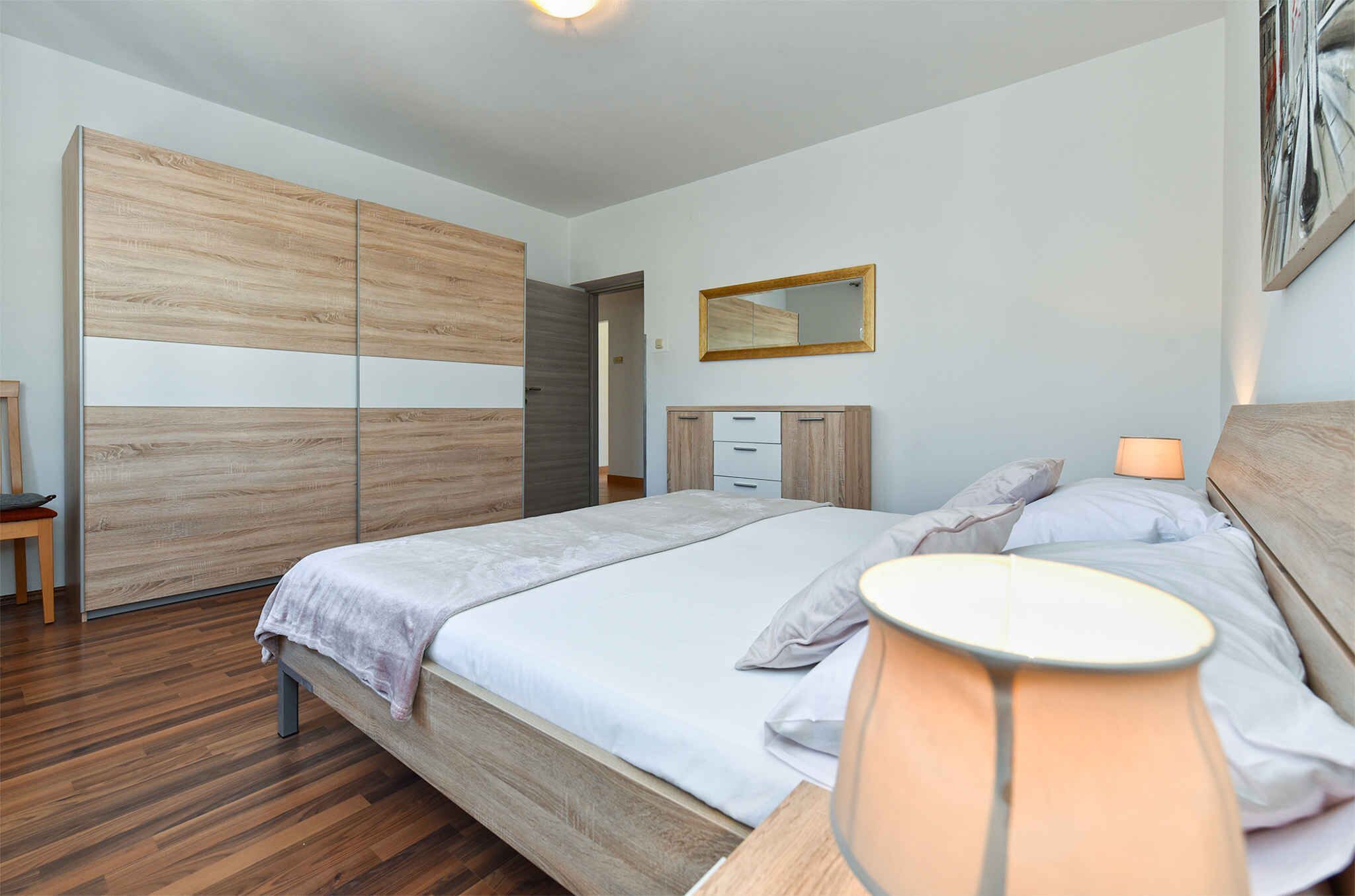 A bedroom with a bed, bedside lamps, a wardrobe, and a mirror.
