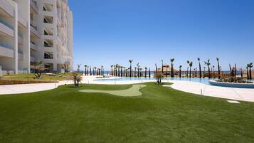 A resort with a swimming pool, palm trees, and a large building with multiple balconies.