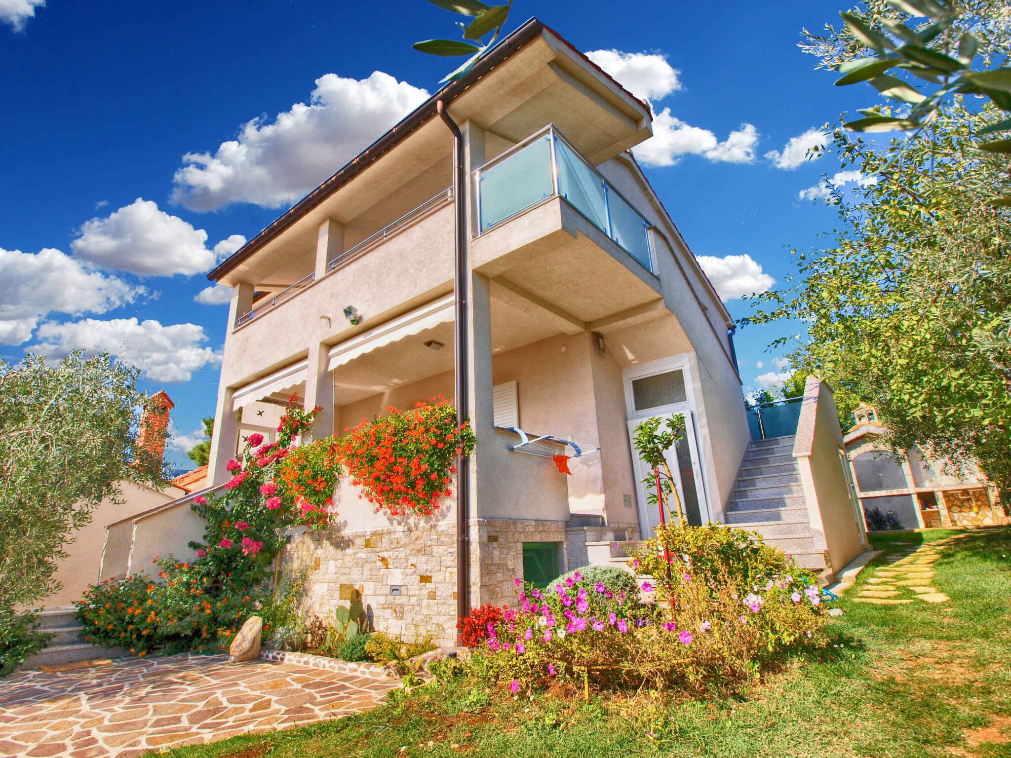 Un edificio a due piani con facciata in pietra, un balcone e un giardino ricco di piante e fiori.