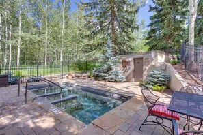 Una piscina al aire libre con escalones, una mesa con mantel a cuadros rojo y blanco, y un pequeño edificio con una puerta.