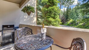 Een terras met een ronde tafel, stoelen, een barbecue en een fles champagne.