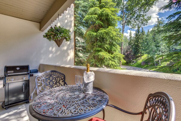 Eine Terrasse mit rundem Tisch, Stühlen, einem Grill und einer Champagnerflasche.