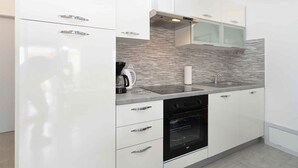 A modern kitchen with white cabinetry, a built-in oven, and a stainless steel sink. - Holiday apartment with garden and barbecue (Fažana)