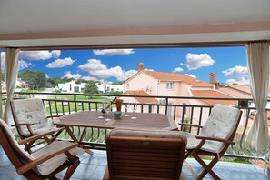 Ein Balkon mit Tisch und Stühlen mit Blick auf ein Wohngebiet, Häuser und einen klaren Himmel.