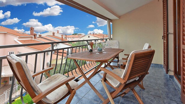 A balcony with a wooden table and chairs, a view of neighboring buildings, and a clear sky. - Holiday apartment with garden and barbecue (Fažana)
