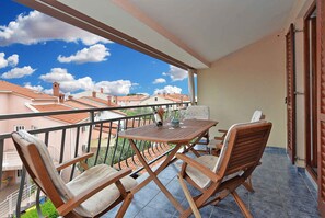 A balcony with a wooden table and chairs, a view of neighboring buildings, and a clear sky. - Holiday apartment with garden and barbecue (Fažana)