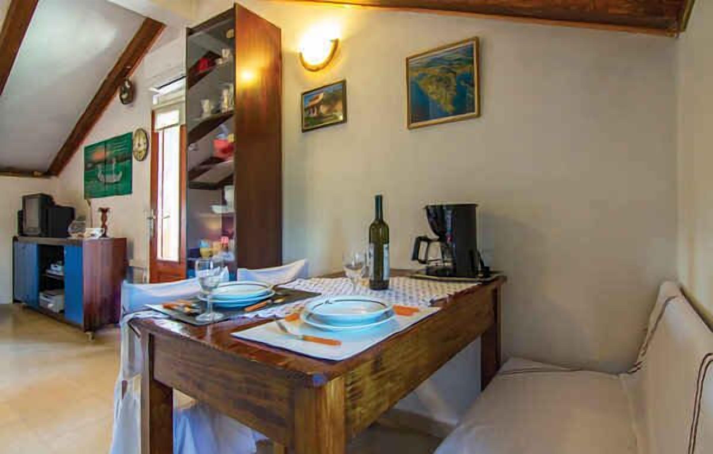 A dining area with a wooden table set for two, a sofa, and a bookshelf.