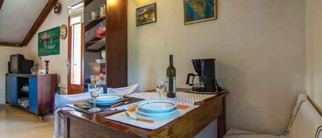 A dining area with a wooden table set for two, a sofa, and a bookshelf.