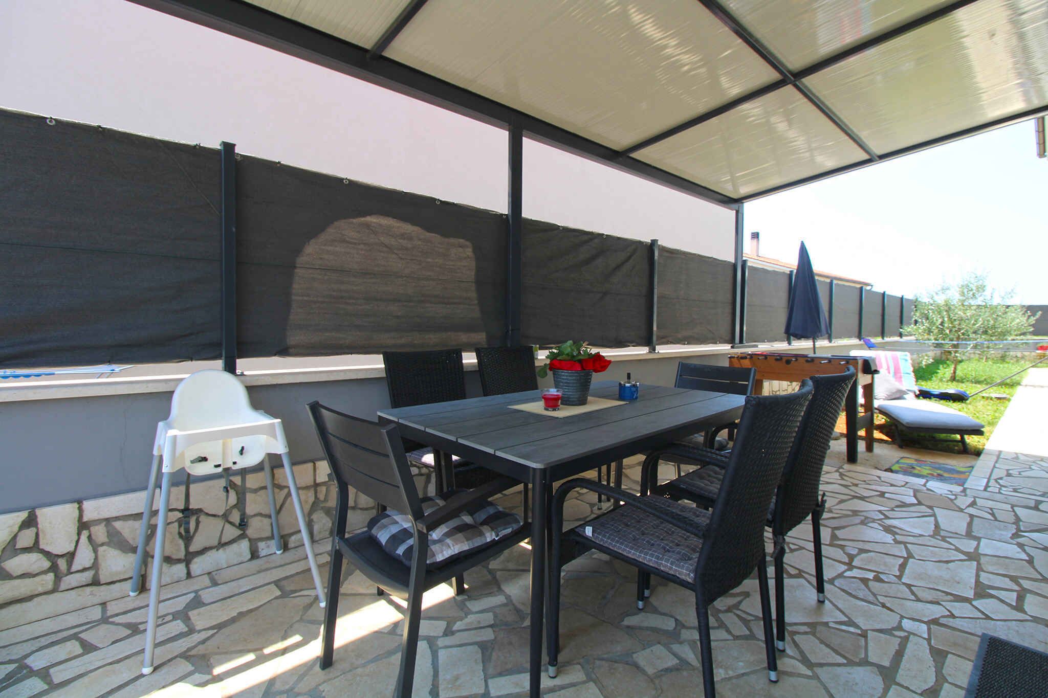 An outdoor patio with a table and chairs, a baby high chair, and a covered area with a view of the garden.