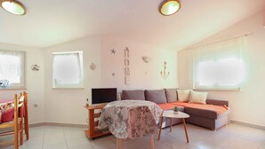 En hyggelig stue med sofa, et lille bord, fjernsyn og et spiseområde med stole.